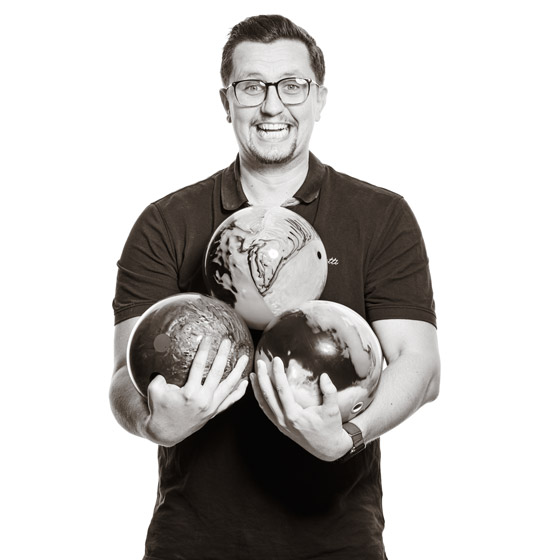 Mario hält drei schwere Bowling-Kugel und lacht.