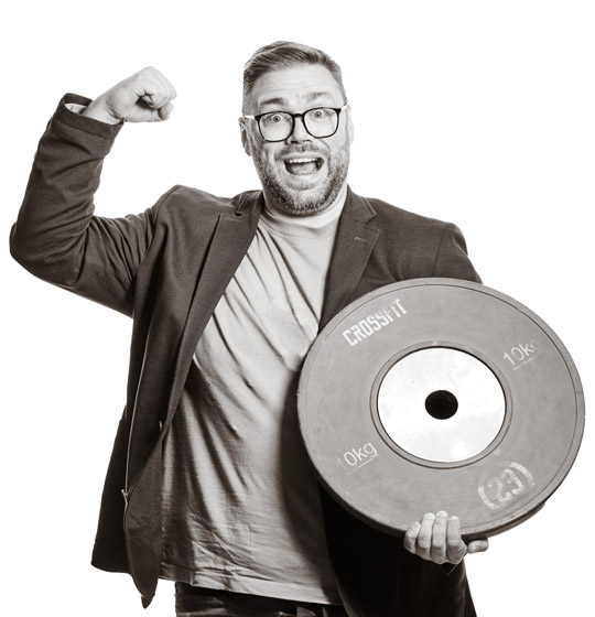 Michael hält eine Gewichtscheibe mit einer Hand und macht mit dem anderen Arm die klassische Pose für Stärke bzw. Muskeln