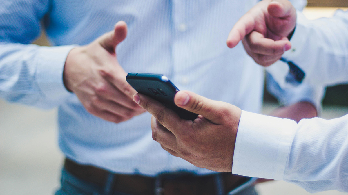 Zwei Personen in Businesskleidung besprechen gemeinsam eine Appentwicklung und betrachten dabei ein Smartphone.