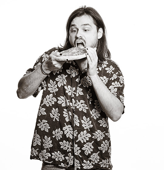 Nicolas reißt den Mund auf, um in die Pizza zu beißen.