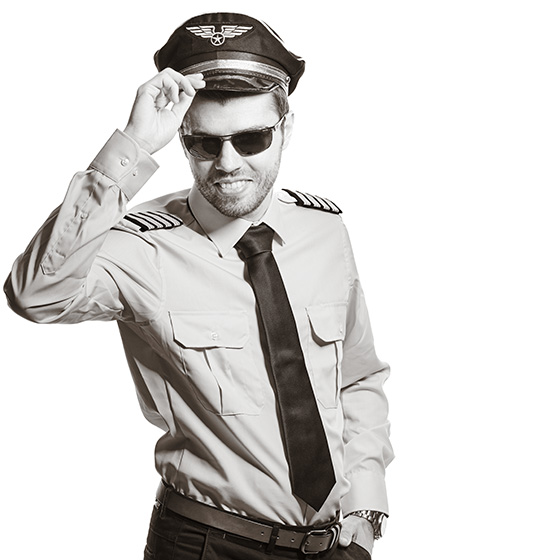 Marco trägt dunkle Sonnenbrillen und hat die Mütze eines Flugkapitäns auf dem Kopf- Mit einer Hand hebt er die Mütze ein wenig an, um zu grüßen.