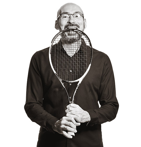 Michael grinst und beißt oben in den Tennisschläger, den er hält