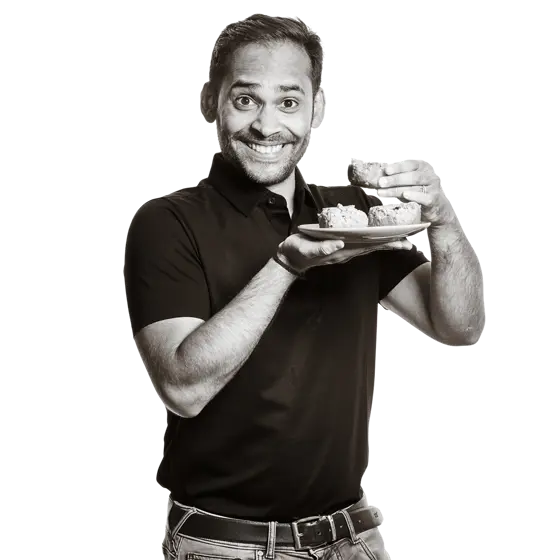 Rajat hält einen Teller mit einer indischen Nachspeise in den Händen. 