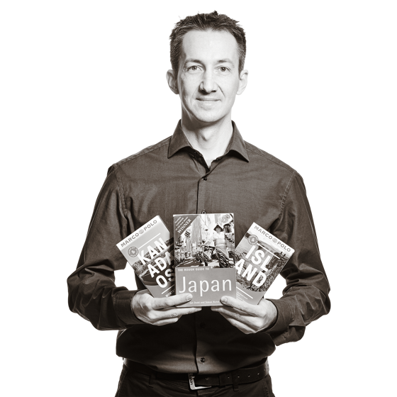 Florian hält drei Bücher aufgefächert vor sich. Es sind Reiseführer für Japan, Kanada und Island. 