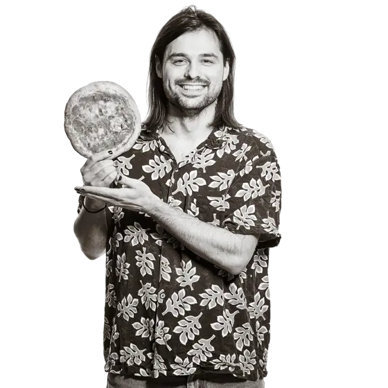 Portrait von Nicolas. Er hält breit lächelnd eine kleine Pizza in die Höhe. 