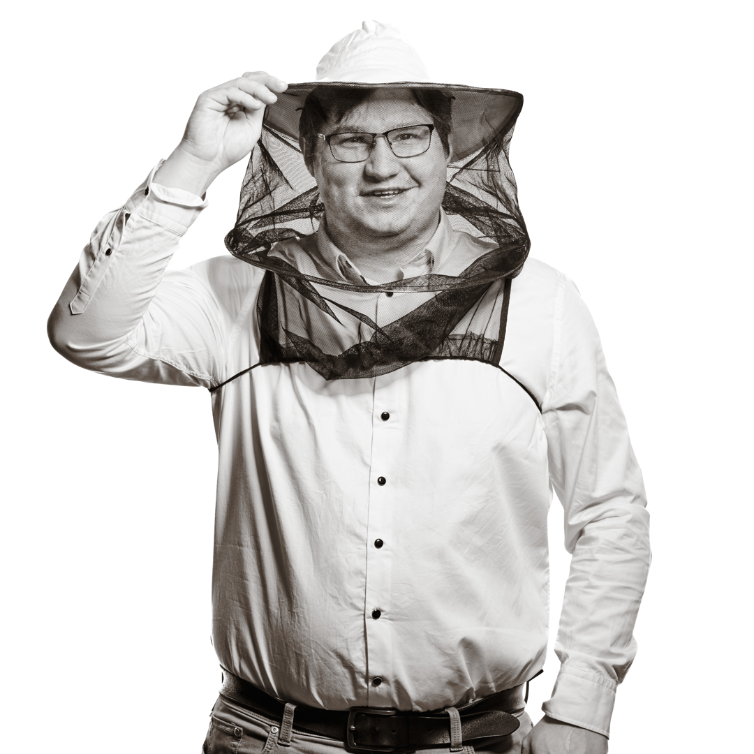 Portrait von Stefan. Er trägt Brille und ein helles Hemd und hält lächelnd eine mit Honig gefüllte Bienenwabe in den Händen.