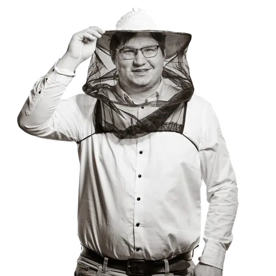 Portrait von Stefan. Er trägt Brille und ein helles Hemd und hält lächelnd eine mit Honig gefüllte Bienenwabe in den Händen.