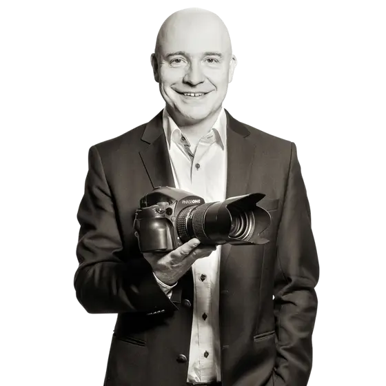 Sven hält eine digitale Fotokamera mit großem Objektiv in der Hand.