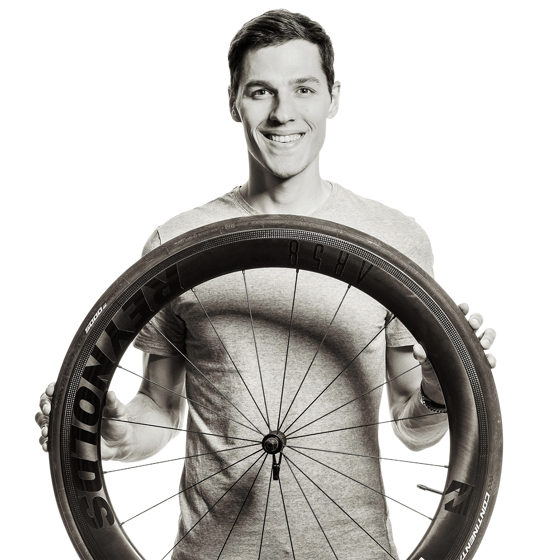 Portrait von Lukas. Er hält einen schwarzen Fahrradreifen vor sich und grinst in die Kamera.