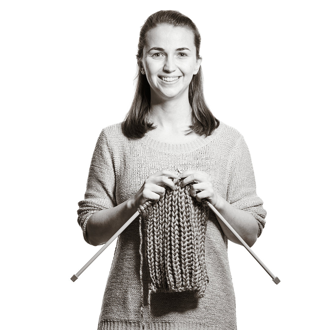 Portrait von Verena. Sie hält zwei Stricknadeln, an denen schon ein Stück fertiger Schal zu sehen ist.