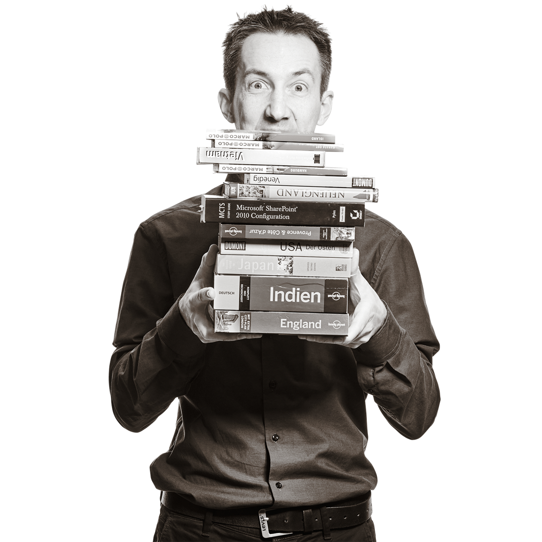 Florian hält drei Bücher aufgefächert vor sich. Es sind Reiseführer für Japan, Kanada und Island. 