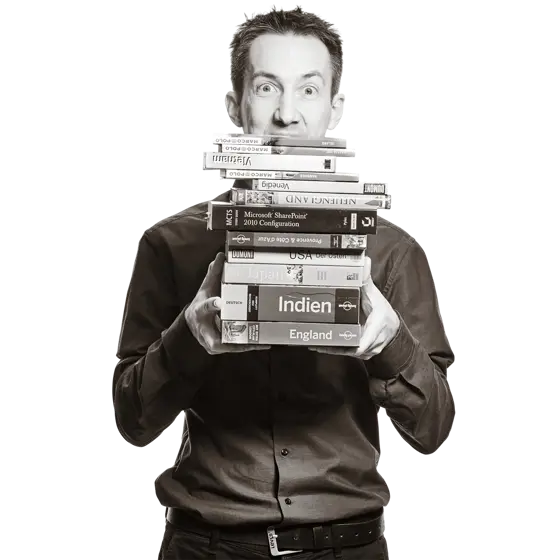 Florian hält drei Bücher aufgefächert vor sich. Es sind Reiseführer für Japan, Kanada und Island. 