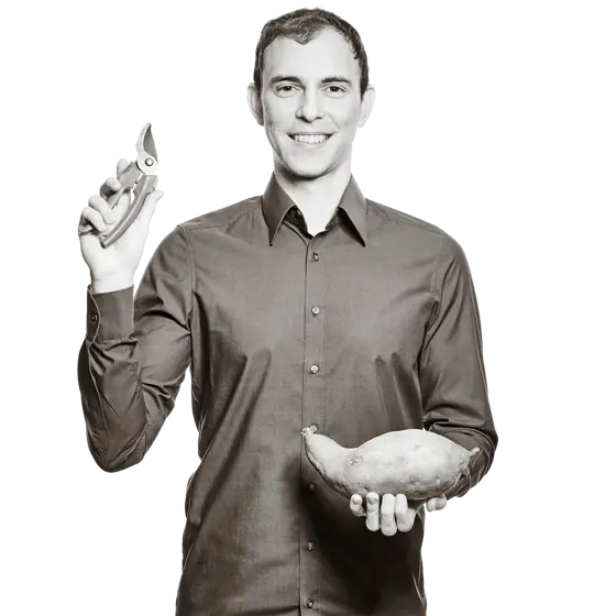 Alexander hält eine Gartenschere in der der einen Hand und eine Süßkartoffel in der anderen. 