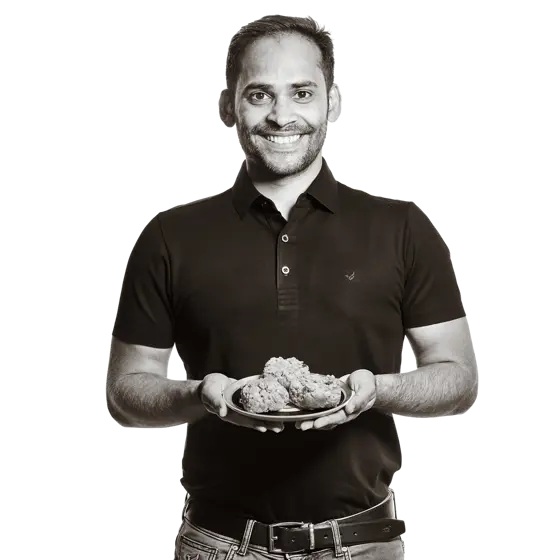 Rajat hält einen Teller mit einer indischen Nachspeise in den Händen. 