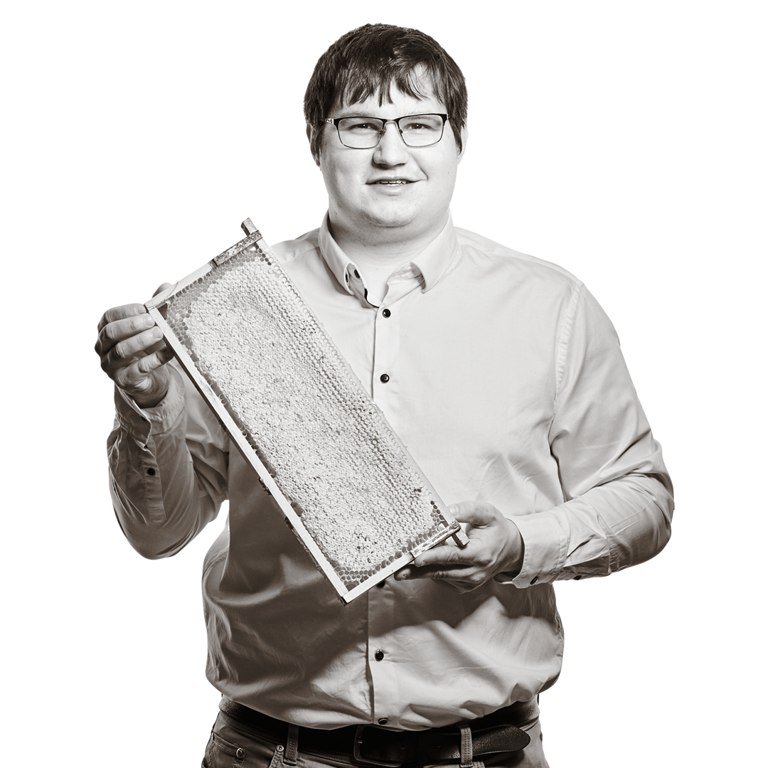 Portrait von Stefan. Er trägt Brille und ein helles Hemd und hält lächelnd eine mit Honig gefüllte Bienenwabe in den Händen.