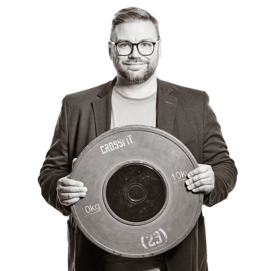 Michael hält eine Gewichtsscheibe. Auf der Scheibe steht "10 kg" und "Crossfit".